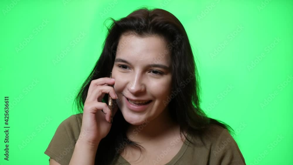 Beautiful young girl with a nice smile on a green background talking on the phone. Beautiful young girl with a nice smile on a green background talking on the phone.