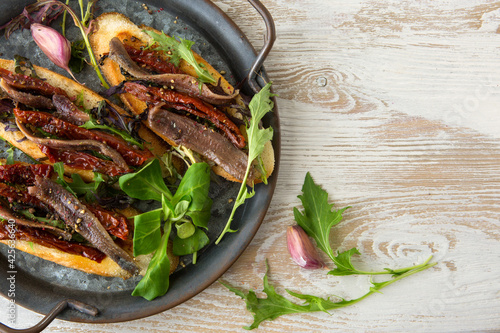 bruschettas with dried tomatoes and anchovies on a tray on a light wooden table