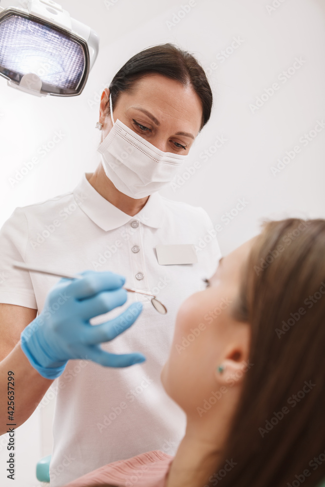 Low angle vertical shot of a professional dentist wearing medical mask and gloves, examining teeth of patient