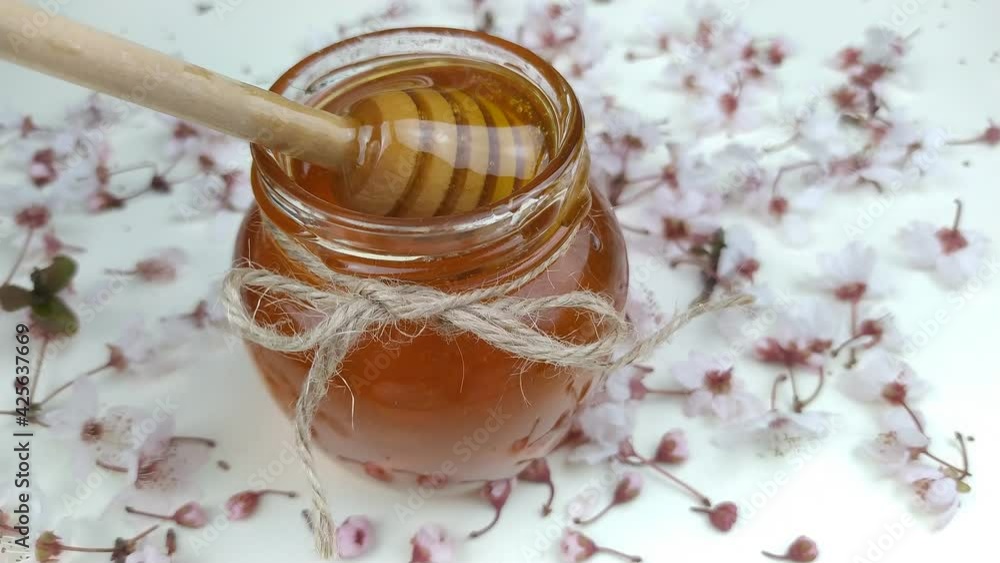 The honey in the glass jar between the flowers is mixed with a wooden mixer. The honey in the glass jar between the flowers is mixed with a wooden mixer.