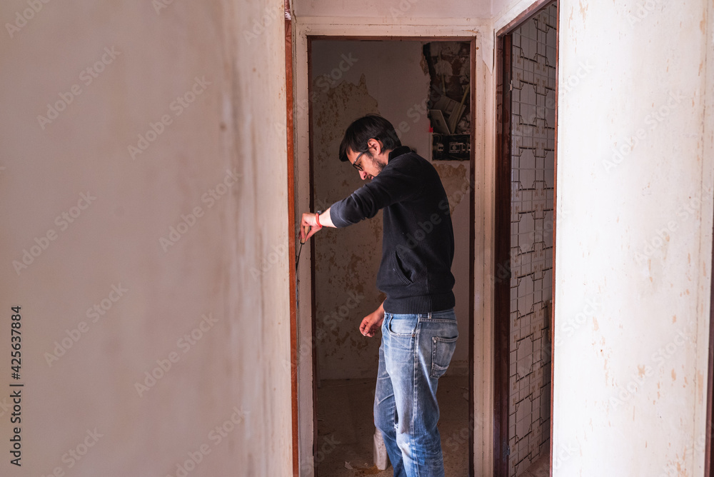 Man removing wallpaper from a hallway wall with a scraper. Works at home Man removing wallpaper from a hallway wall with a scraper. Works at home