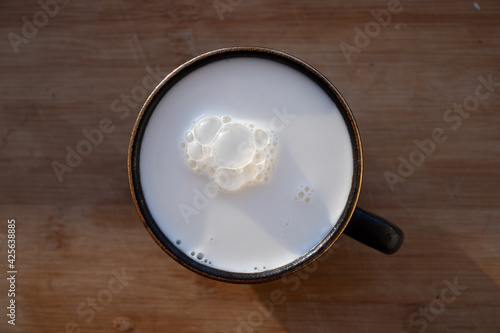 Glass of milk standing on old wooden table. Black glass with white milk. Black glass with white milk on the table