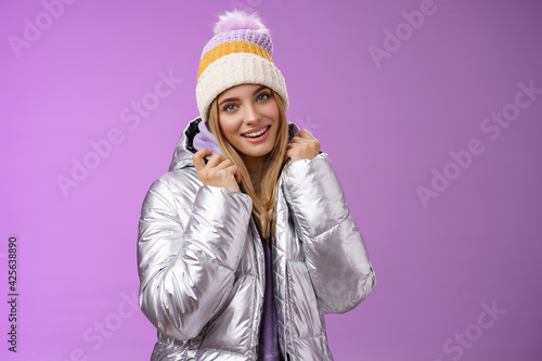 Tender feminine gentle blond girlfriend posing boyfriend take pictures ski resort holiday wearing glittering stylish jacket winter hat standing pleased purple background smiling delighted photo