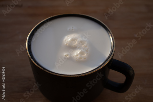Glass of milk standing on old wooden table. Black glass with white milk. Black glass with white milk on the table
