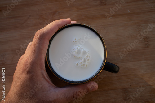 Glass of milk standing on old wooden table. Black glass with white milk. Black glass with white milk on the table