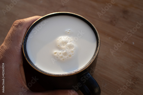 Glass of milk standing on old wooden table. Black glass with white milk. Black glass with white milk on the table