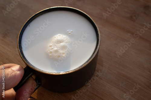 Glass of milk standing on old wooden table. Black glass with white milk. Black glass with white milk on the table