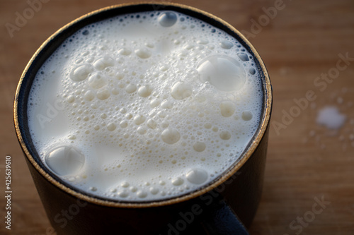 Glass of milk standing on old wooden table. Black glass with white milk. Black glass with white milk on the table