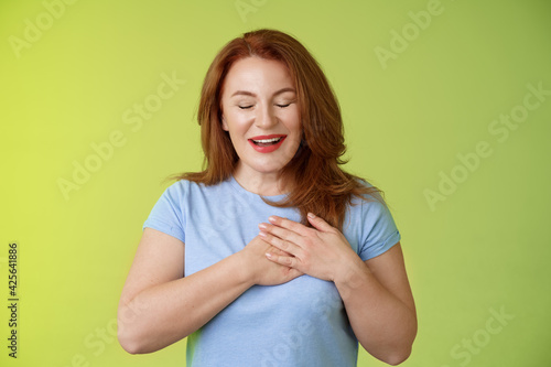 Fascinated cute redhead passionate middle-aged woman sighing lovely touch heart close eyes smiling delighted express admiration temptation feeling appreciation grateful emotions green background