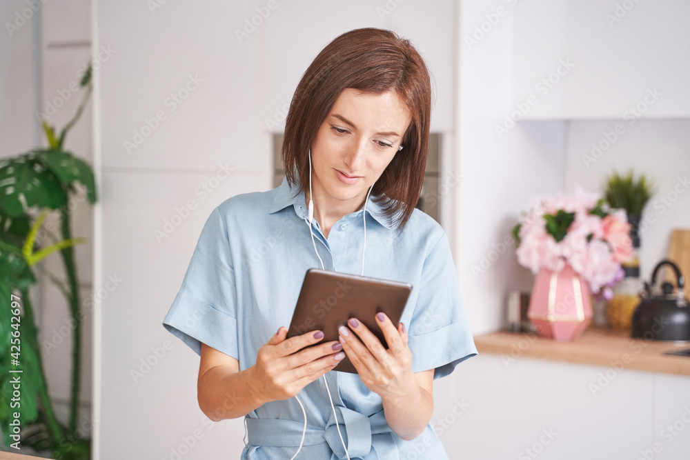 Young woman sitting at kitchen. Working on tablet. Online study concept. Safety lockdown distance teaching. Female person. Quarantine office. Business writer. Video relax Young woman sitting at kitchen. Working on tablet. Online study concept. Safety lockdown distance teaching. Female person. Quarantine office. Business writer. Video relax