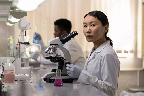 Portrait of Asian young woman looking at camera while sitting at the table and using microphone at work in the lab