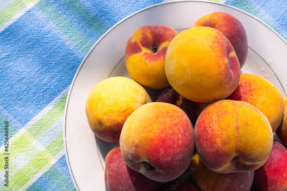 Delicious and flavorful fresh peaches on a white plate on a table with blue tablecloth outdoors Delicious and flavorful fresh peaches on a white plate on a table with blue tablecloth outdoors