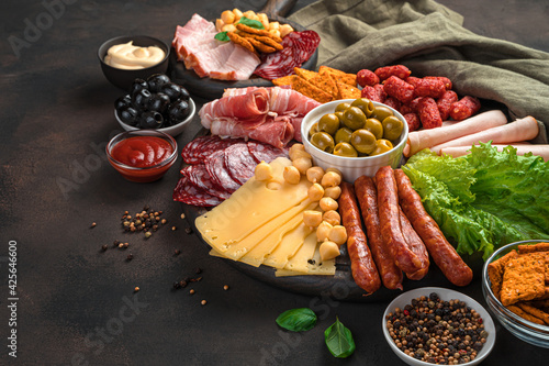 Meat and cheese snacks with salad and olives on a brown background.