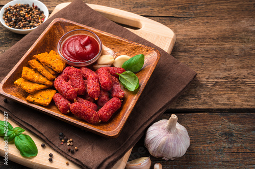 Wooden plate with smoked, garlic mini sausages and tomato crackers close-up on a brown wooden background. photo