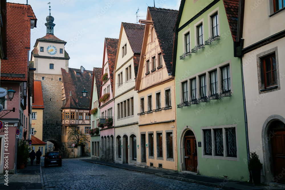 Medieval narrow street, colorful renaissance and gothic historical buildings, White Tower or Weisser Turm, sunny autumn day, old town, Rothenburg ob der Tauber, Bavaria, Germany