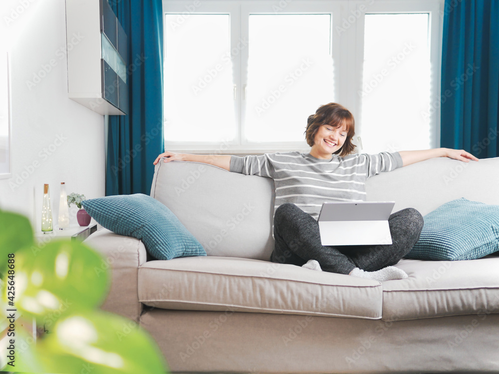 Smiling girl sit relax on couch using modern laptop.happy young woman freelance work on computer from home. social-distancing and self-isolation concept. coronavirus stay home and online live.