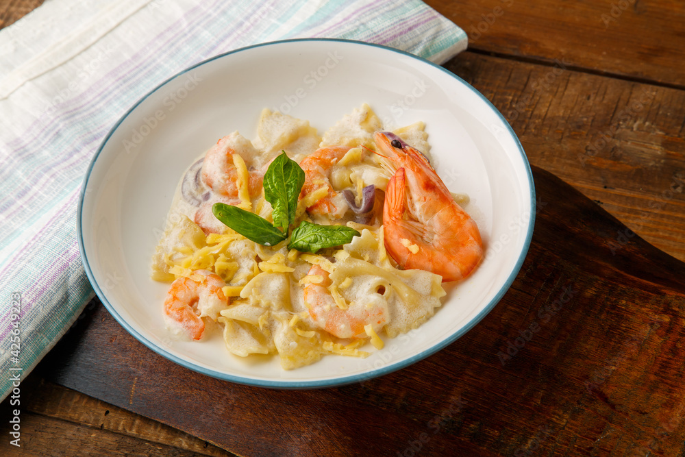 Pasta with shrimps in a creamy sauce, decorated with spinach on a gray plate on a wooden table on a napkin.