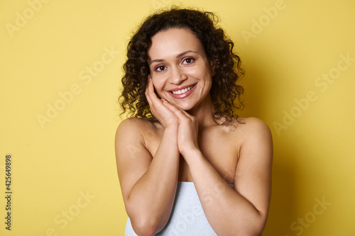 Portrait of beautiful young smiling woman with curly short hair, looking at camera while posing over yellow background with copy space
