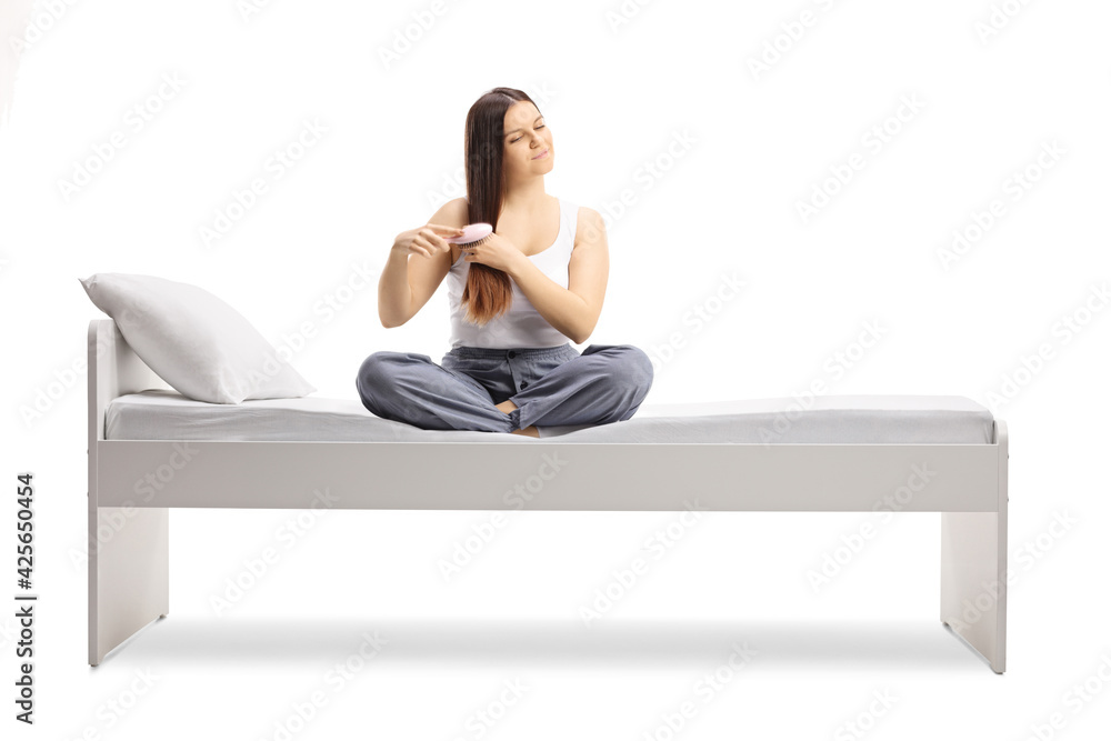 Young woman in pajamas sitting on a bed and brushing her hair Young woman in pajamas sitting on a bed and brushing her hair