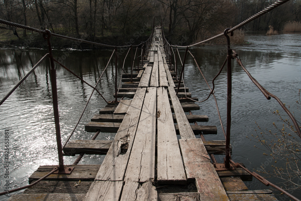 Wooden suspension bridge on the river. Springtime.