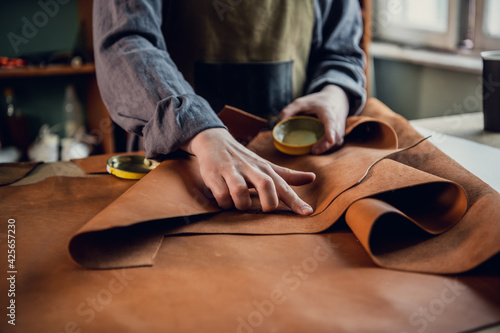 Before making shoes out of leather, a young guy lays them out on the table in the workshop