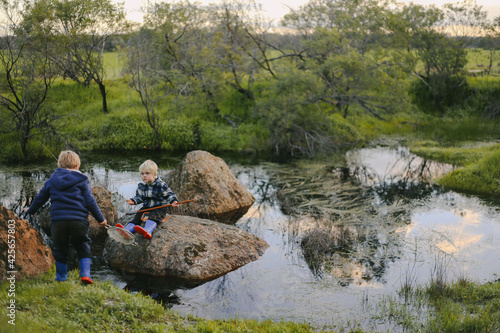 Children sitting on rocks using nets to catch tadpoles in dark fresh water hole