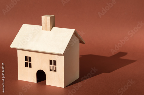 Home, sweet home. Wooden house building miniature model with shadow on brown background. Buying new apartment, mortgage, business real estate insurance concept. New property, family life