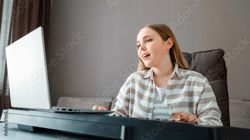 Canvas Print Woman learns music singing vocals playing piano online using laptop at home interior