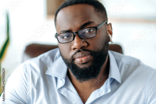 Close-up portrait of an attractive confident successful intelligent serious african american bearded man with glasses, wearing a stylish formal shirt, concentrated looking at the camera