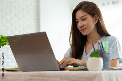 Asian woman working on a laptop sitting on the bed in the house.