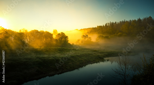 A beautiful spring landscape of a river valley with morning mist. Springtime scenery of a river flowing through the forest. Water evaporating in sun rays. Springtime scenery of Northern Europe.