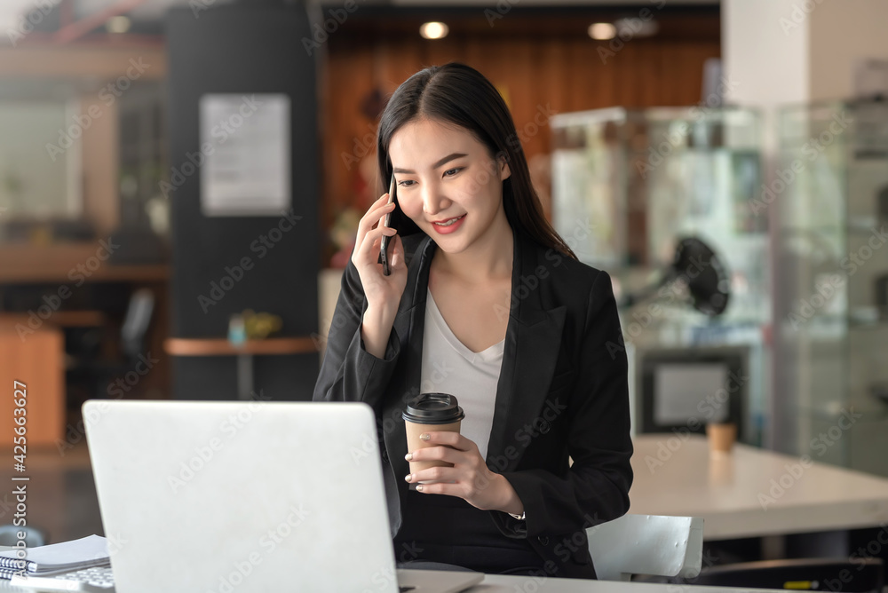 Beautiful Asian businesswoman talking on the phone and holding coffee while chatting with customers in the office. Beautiful Asian businesswoman talking on the phone and holding coffee while chatting with customers in the office.