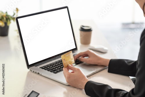 Close up. Businesswoman hand holding credit card shopping online by using a laptop blank white screen at the office.