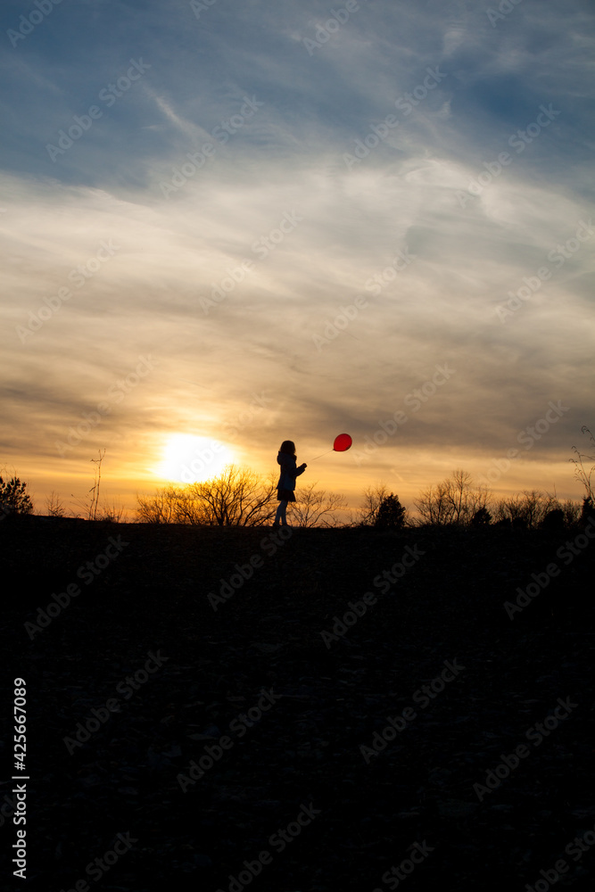 Girl with red balloon at sunset