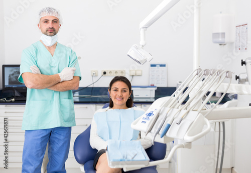 Portrait of positive dentist and happy cute woman sitting in dental chair after teeth cure