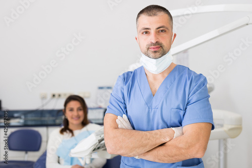 A portrait of a dentist in face mask with patient in the background at dental clinic