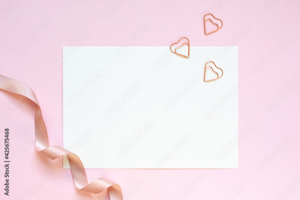 White invitation a5 card mockup with three hearted shape clips and satin tape on a pink table. White invitation a5 card mockup with three hearted shape clips and satin tape on a pink table.