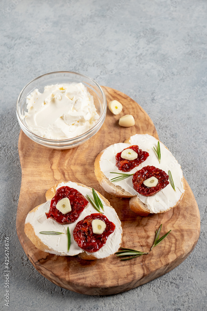 Homemade sandwiches with cream cheese and sun-dried tomatoes on a wooden board of olive - delicious healthy breakfast, vertical image, copy space