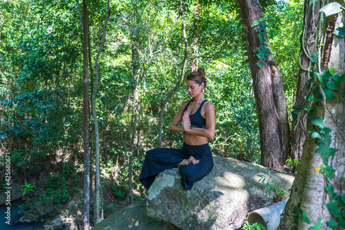 Young caucasian brunette girl is meditating in nature at tropical garden in summer, Thailand