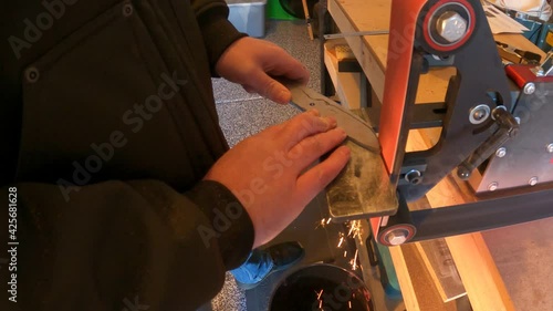 Man using a belt grinder to cut a knife out of bar steel with sparks flying - slow motion photo