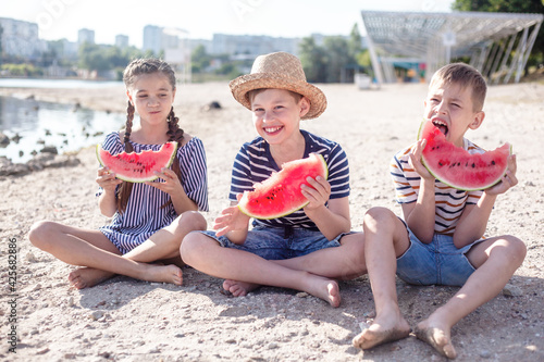 Group of preteen kids dressed fashion summer clothes eat watermelon in the beach and eat with fruits photo