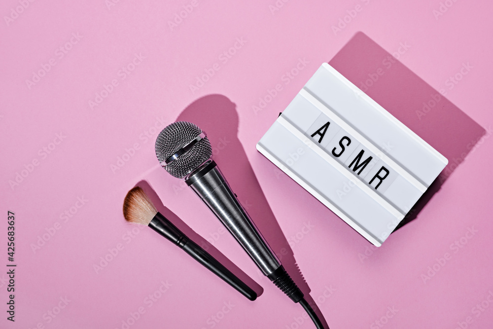 Microphone, brush and ASMR text lightbox on pink background. ASMR recording stress relieving sounds concept, flat lay, trending shadows Microphone, brush and ASMR text lightbox on pink background. ASMR recording stress relieving sounds concept, flat lay, trending shadows