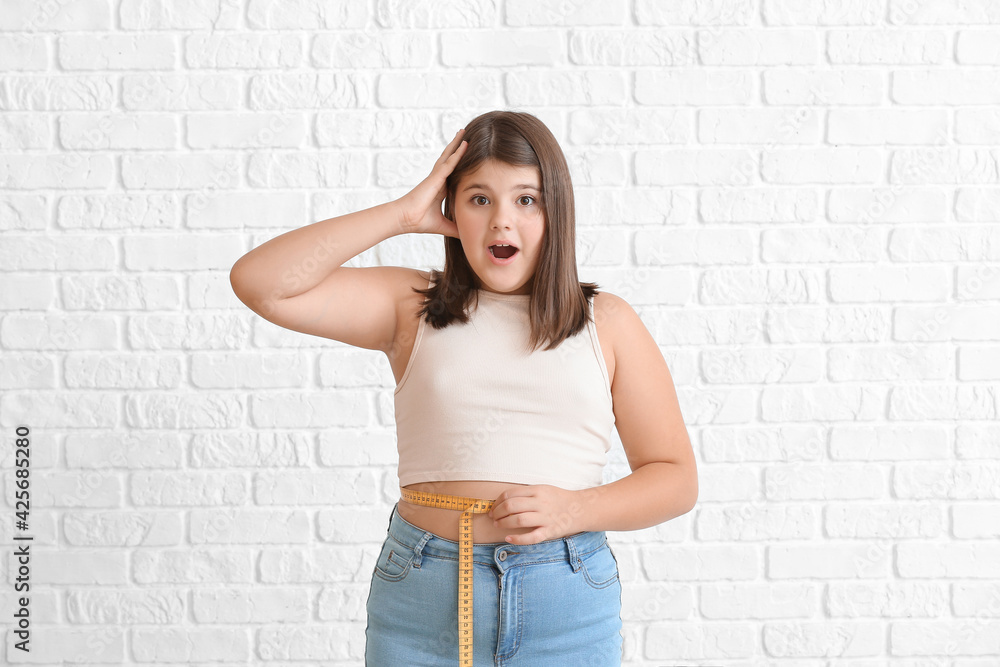 Shocked overweight girl measuring her waist on white brick background Shocked overweight girl measuring her waist on white brick background