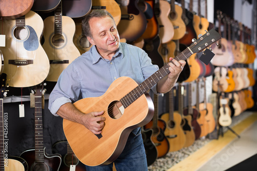 Smiling guitarist is playing on modern acoustic guitar in music shop.