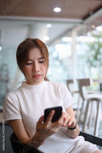 Portrait of asian woman sitting in modern workplace and using mobile phone.