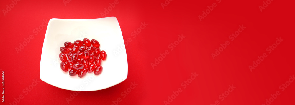 Krill oil capsules.banner. Red gelatin capsules with krill oil in a white ceramic cup on a  red background .Dietary supplements and vitamins banner.omega fatty acids