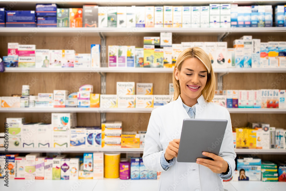 Portrait of smiling female caucasian pharmacist standing in drug store holding tablet computer.