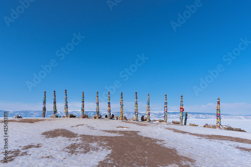 A row of high ritual cult pillars of the Buryats, tied with multi-colored ribbons, on a clear winter day. Sacred Cape Burkhan, Shamanka rock, lake Baikal, Siberia, Russia