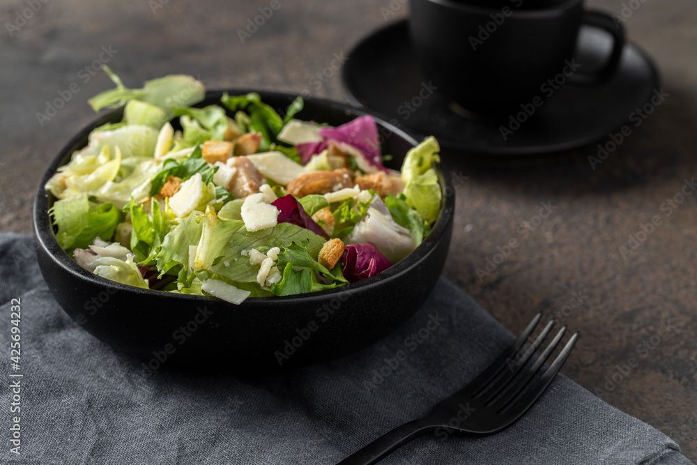 Caesar salad in the black plate on cocnrete background made with different lettuce, croutons, parmesan and chicken Caesar salad in the black plate on cocnrete background made with different lettuce, croutons, parmesan and chicken