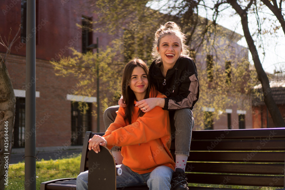 Two teenage skater girls are hanging out in the neighborhood, chatting and smiling at each other. Two teenage skater girls are hanging out in the neighborhood, chatting and smiling at each other.